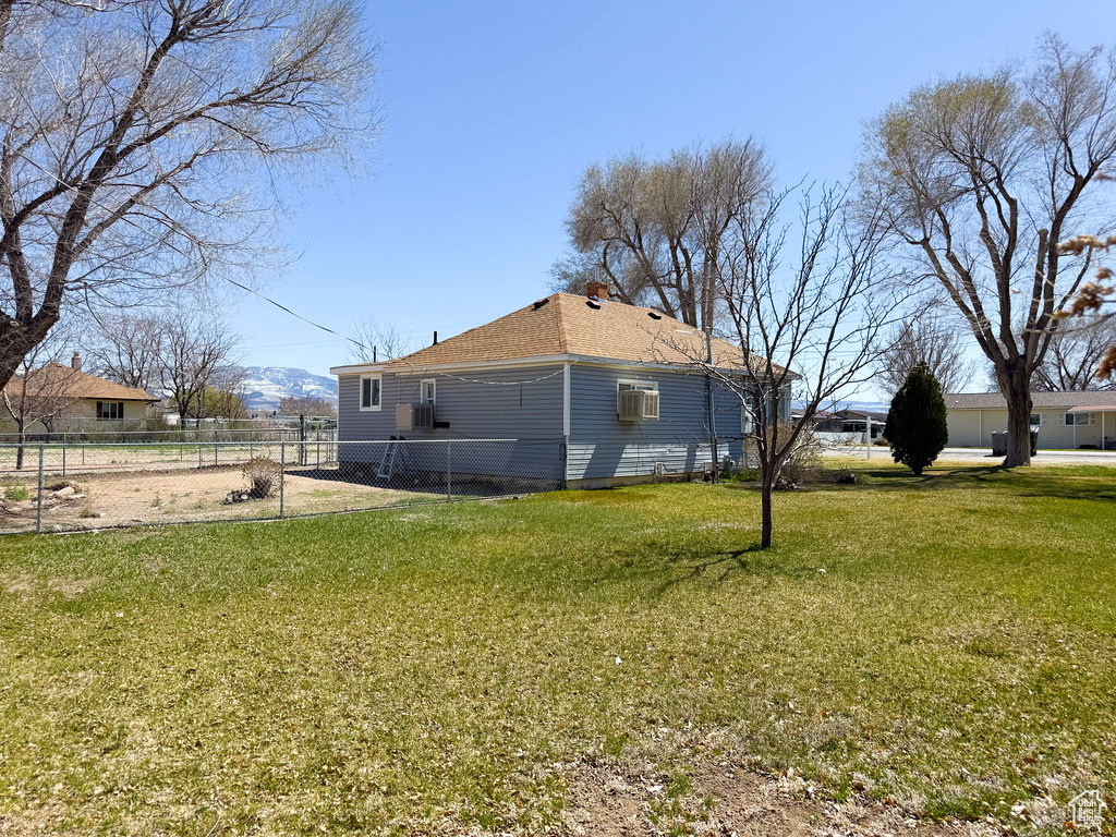 View of property exterior with a shingled roof, fence, and a lawn