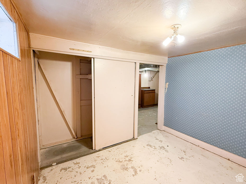 Unfurnished bedroom featuring wallpapered walls, concrete flooring, and a closet