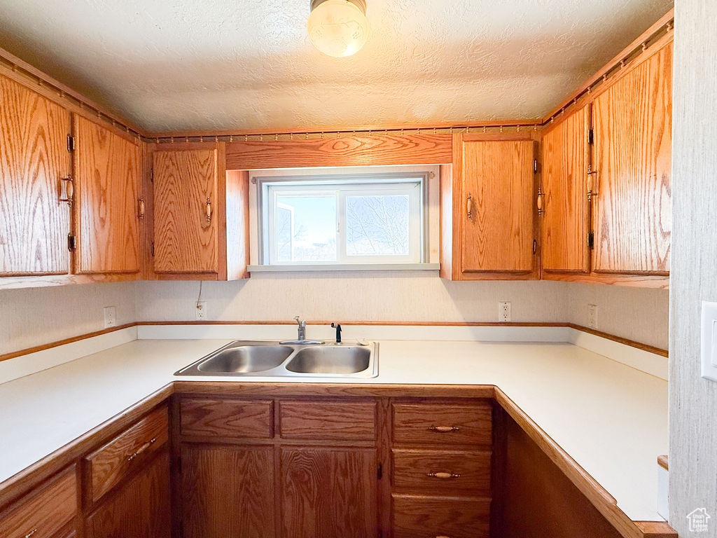 Kitchen with light countertops, a textured ceiling, a sink, and brown cabinetry