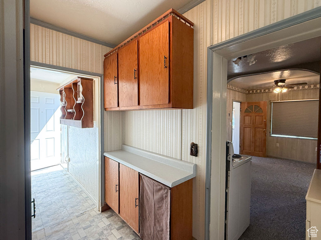 Kitchen featuring crown molding, ceiling fan, brown cabinetry, light countertops, and wallpapered walls
