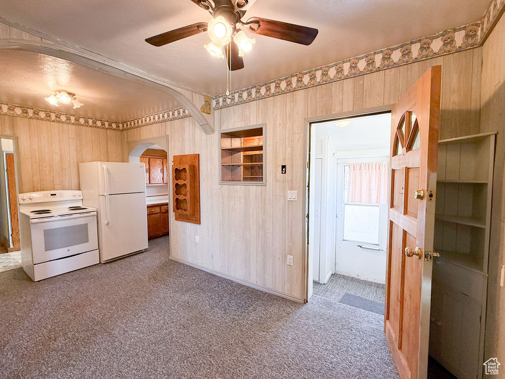 Kitchen with white appliances, wood walls, ceiling fan, arched walkways, and carpet