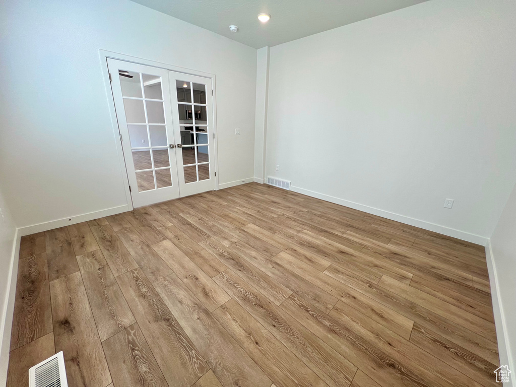 Empty room with baseboards, light wood-style flooring, visible vents, and french doors