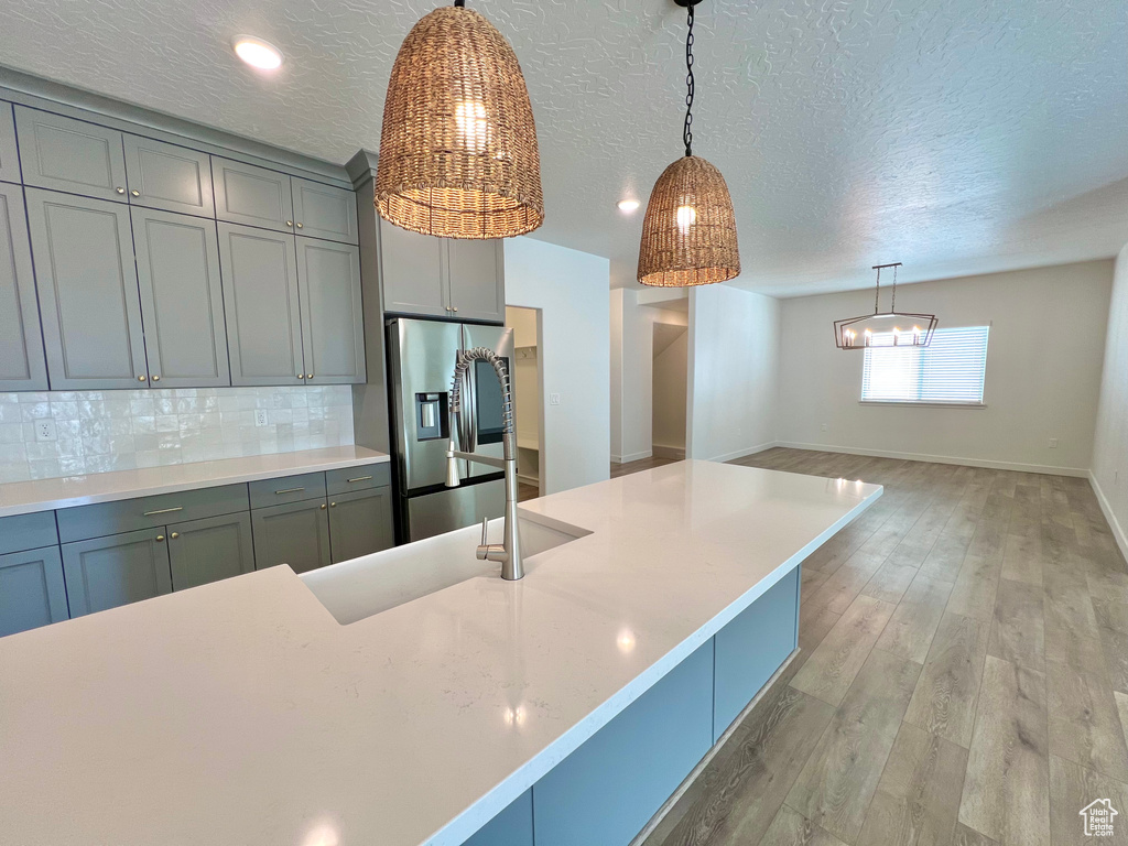 Kitchen featuring light countertops, light wood finished floors, stainless steel fridge, decorative light fixtures, and decorative backsplash