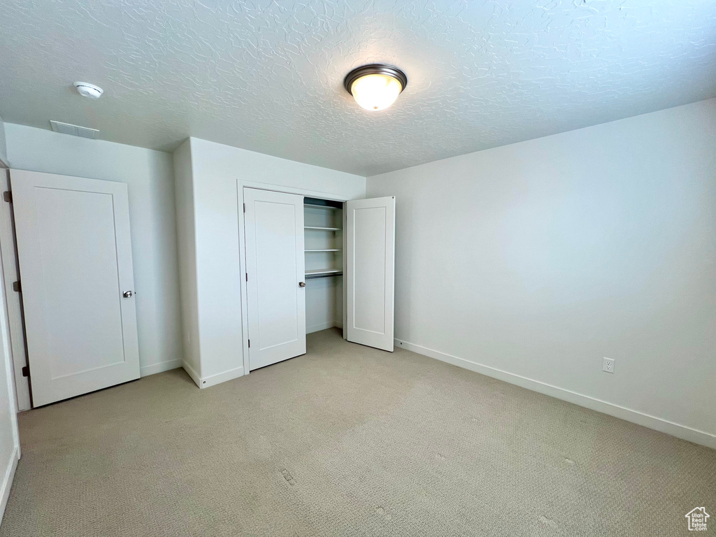 Unfurnished bedroom with a closet, a textured ceiling, baseboards, and light colored carpet