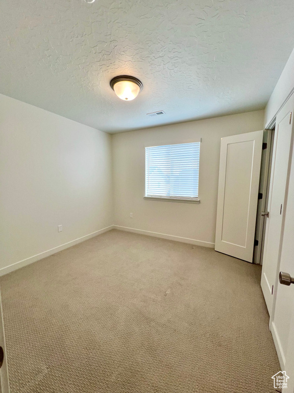 Unfurnished bedroom with light carpet, baseboards, visible vents, and a textured ceiling