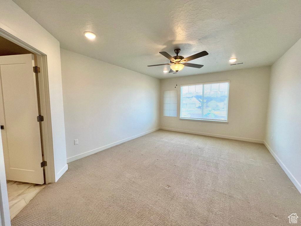 Spare room with light carpet, baseboards, a textured ceiling, and a ceiling fan