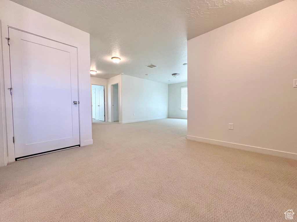 Unfurnished room featuring a textured ceiling, baseboards, light colored carpet, and visible vents