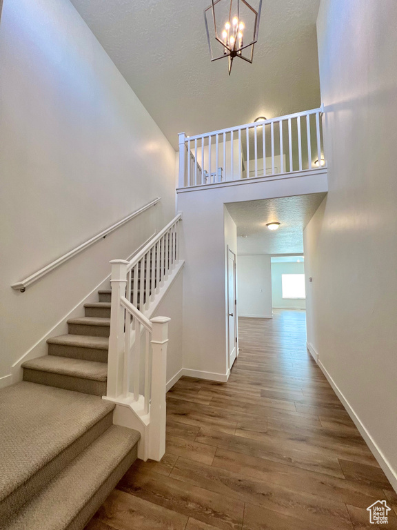 Stairway featuring baseboards, a textured ceiling, wood finished floors, and an inviting chandelier