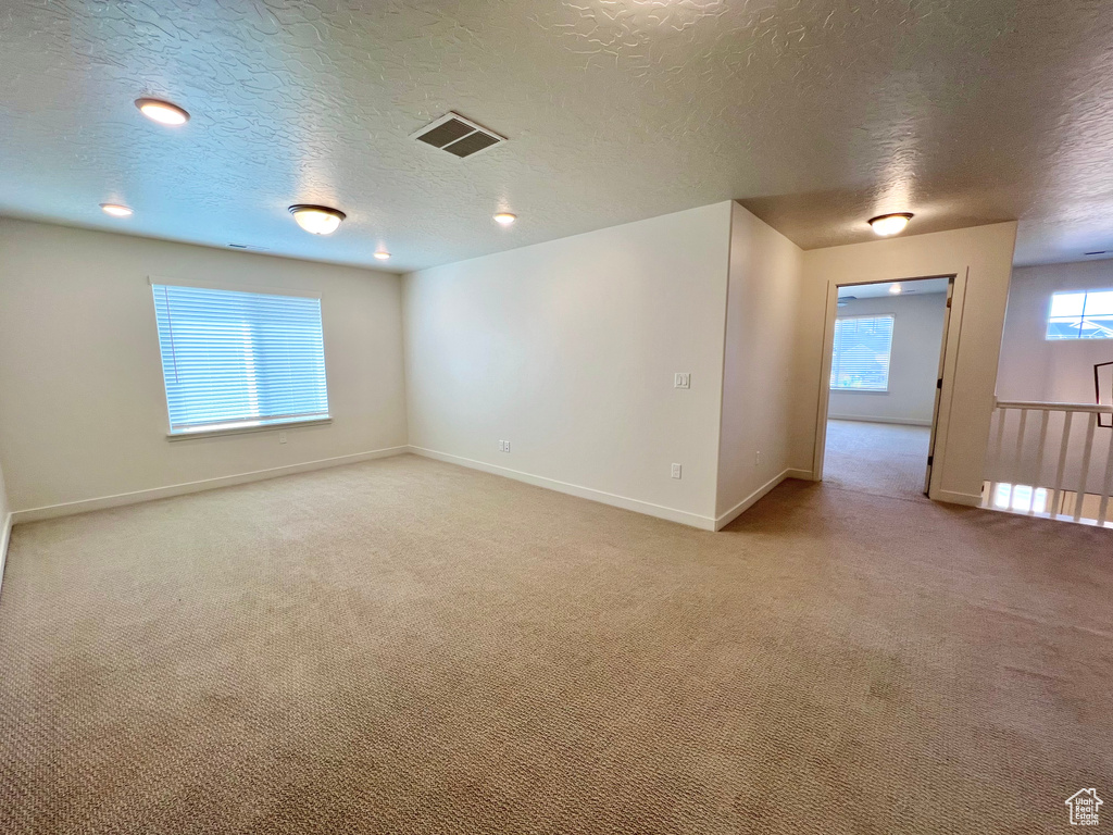 Empty room featuring light carpet, baseboards, visible vents, and a textured ceiling