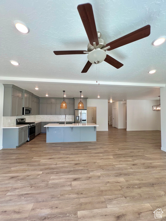 Kitchen with light countertops, appliances with stainless steel finishes, gray cabinetry, open floor plan, and ceiling fan