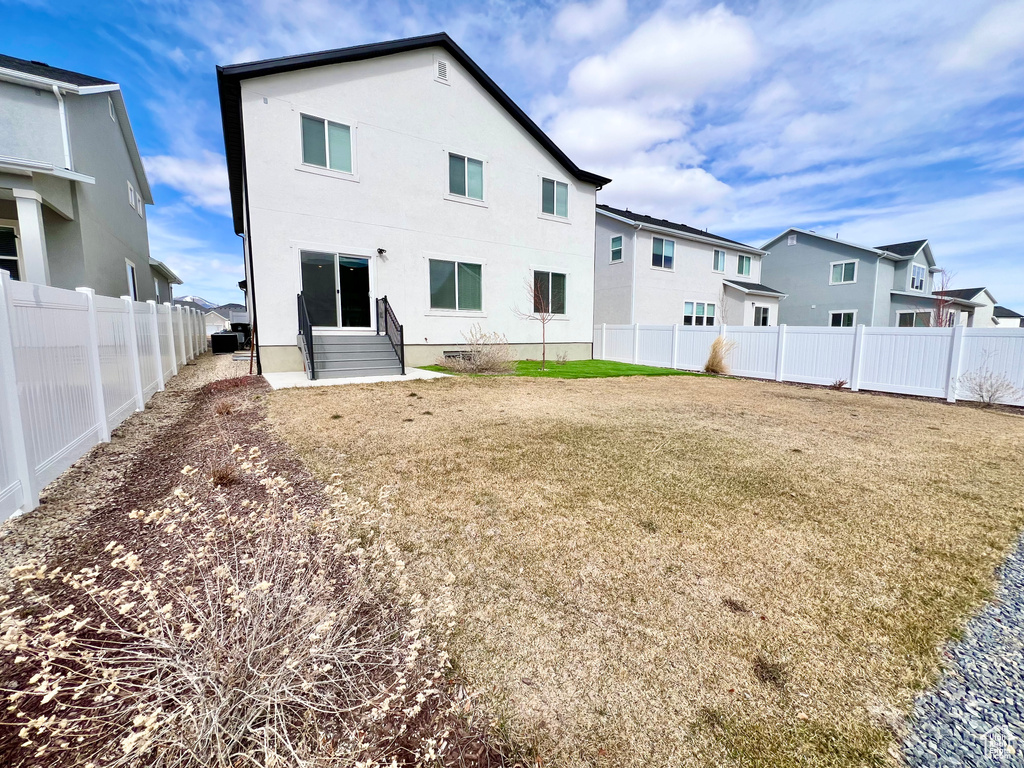 Rear view of property featuring stucco siding, a fenced backyard, crawl space, entry steps, and a lawn