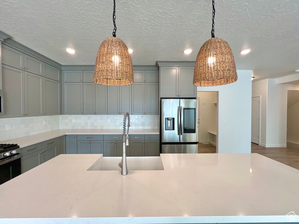 Kitchen featuring decorative backsplash, light countertops, stainless steel fridge, a sink, and gray cabinets