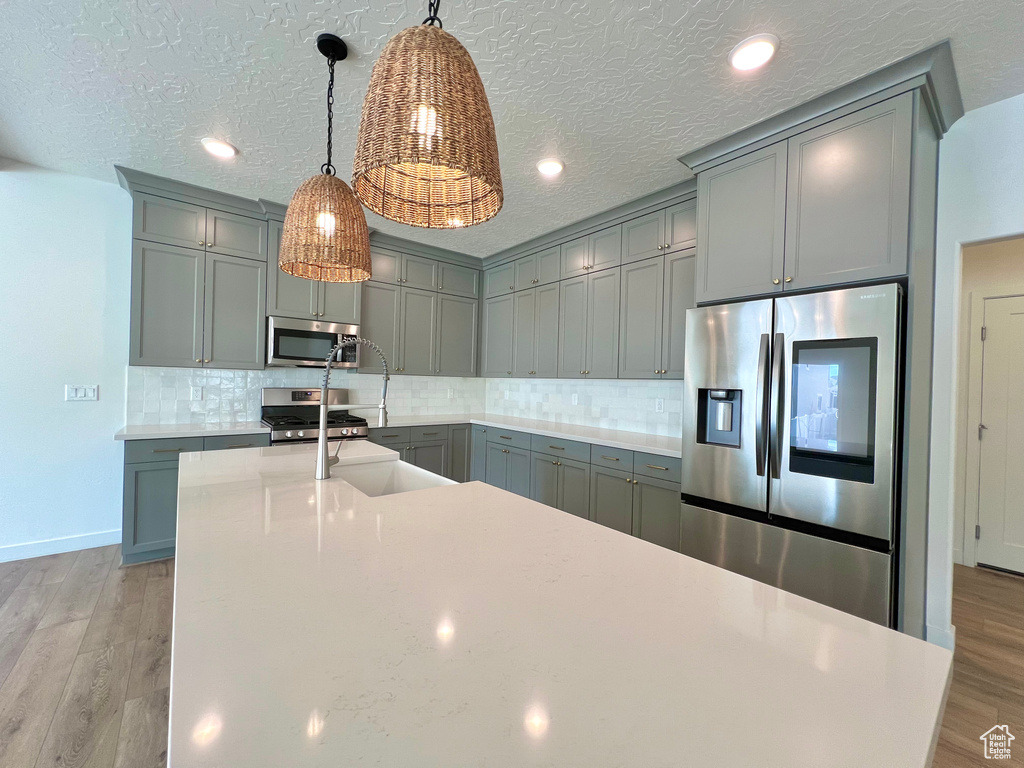 Kitchen featuring gray cabinets, tasteful backsplash, light wood-type flooring, and appliances with stainless steel finishes