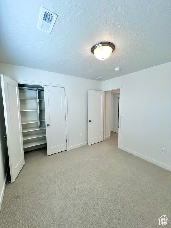 Unfurnished bedroom with a closet, light carpet, baseboards, and visible vents