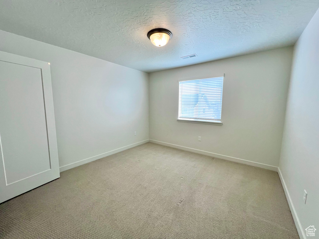 Unfurnished room featuring visible vents, baseboards, light colored carpet, and a textured ceiling