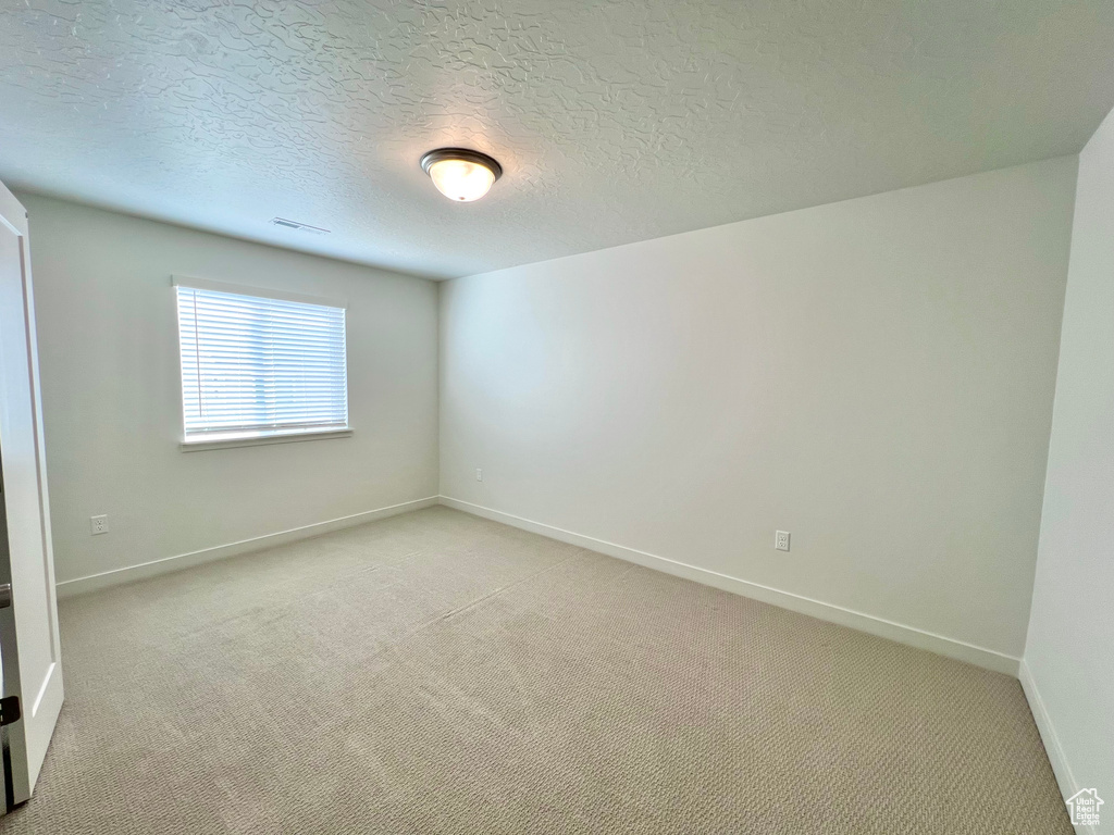 Empty room featuring baseboards, a textured ceiling, visible vents, and light colored carpet
