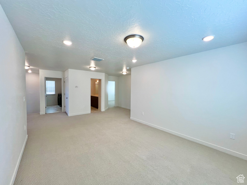 Empty room with visible vents, light carpet, baseboards, and a textured ceiling