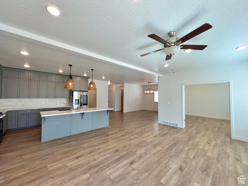 Kitchen featuring open floor plan, gray cabinets, stainless steel fridge with ice dispenser, ceiling fan with notable chandelier, and light wood-style floors