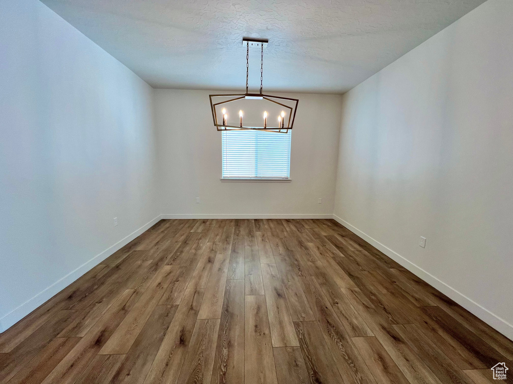 Unfurnished dining area with baseboards, a textured ceiling, wood finished floors, and a chandelier