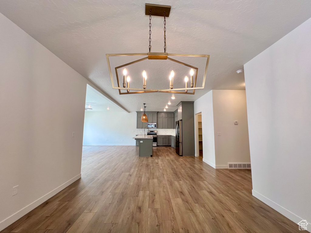 Interior space with light wood finished floors, baseboards, a notable chandelier, and visible vents