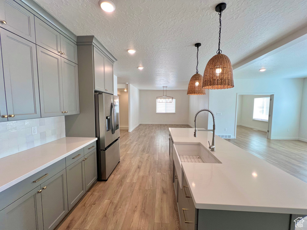 Kitchen with stainless steel fridge with ice dispenser, light countertops, a sink, and gray cabinets