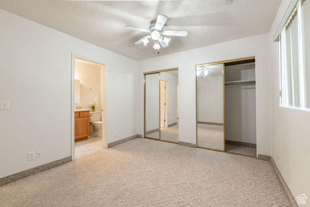 Unfurnished bedroom with baseboards, light carpet, ensuite bath, a textured ceiling, and two closets