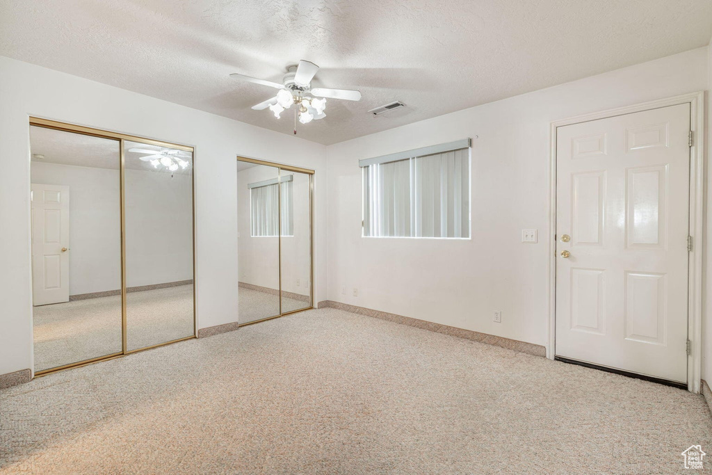 Unfurnished bedroom with visible vents, carpet, two closets, and a textured ceiling