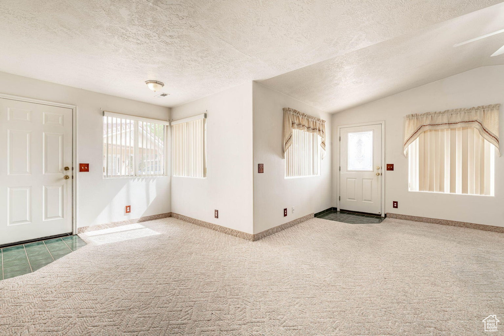 Carpeted foyer entrance with visible vents, baseboards, vaulted ceiling, and a textured ceiling