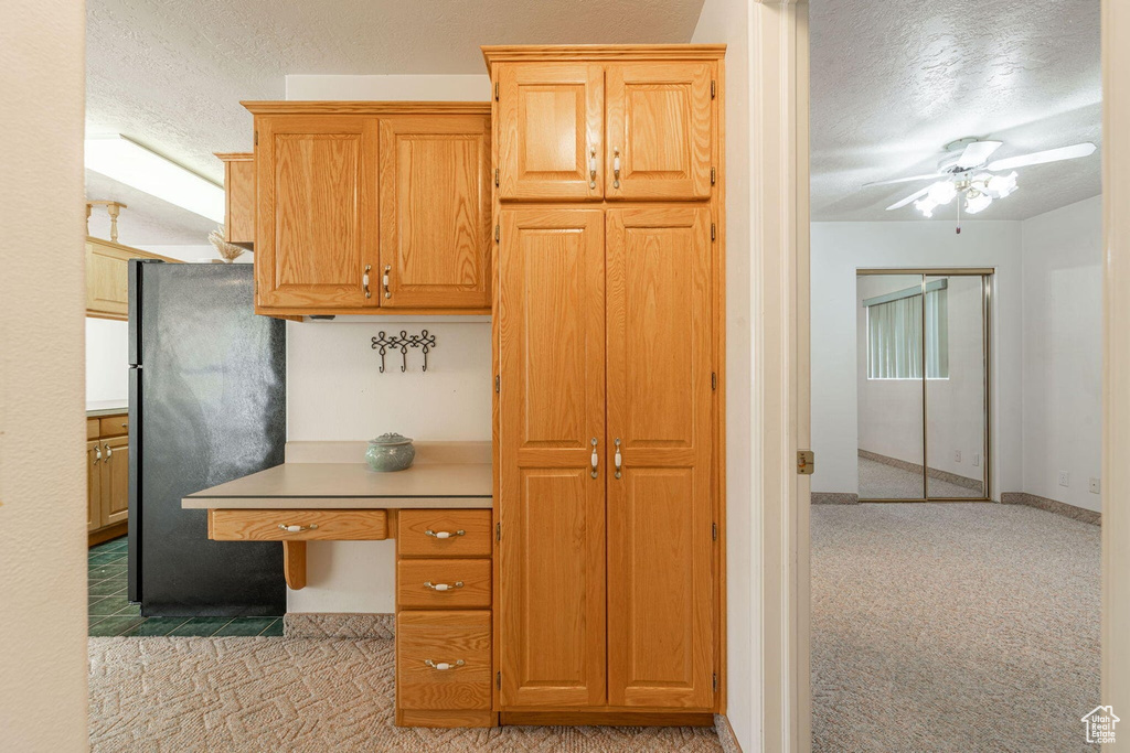 Kitchen featuring light countertops, freestanding refrigerator, a ceiling fan, a textured ceiling, and light colored carpet