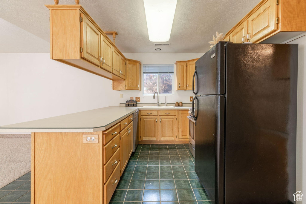 Kitchen with a sink, light countertops, freestanding refrigerator, a peninsula, and dishwashing machine