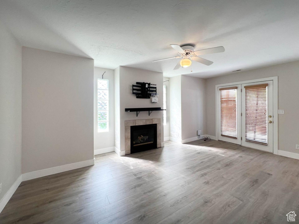 Unfurnished living room featuring wood finished floors, ceiling fan, a tiled fireplace, and baseboards
