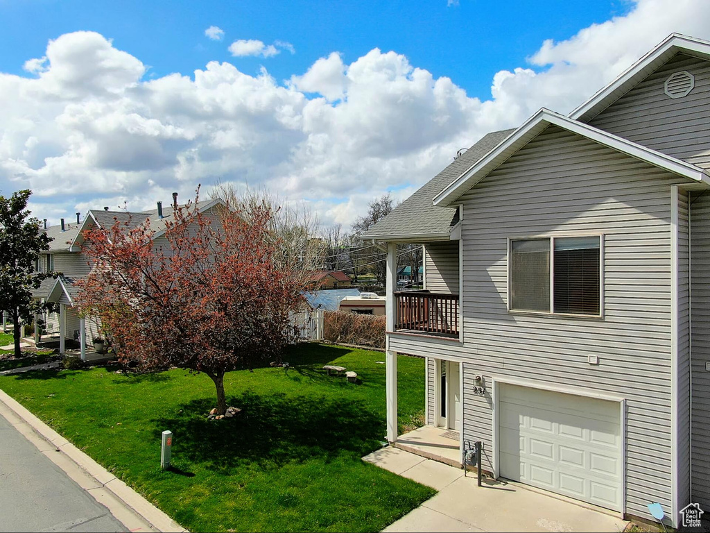 View of side of property with an attached garage, a shingled roof, driveway, and a lawn