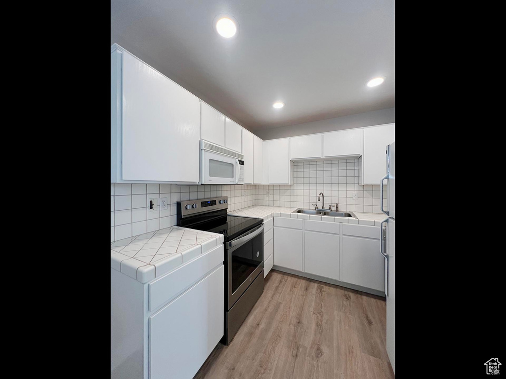 Kitchen featuring white microwave, light wood-style flooring, stainless steel electric range oven, a sink, and tile counters