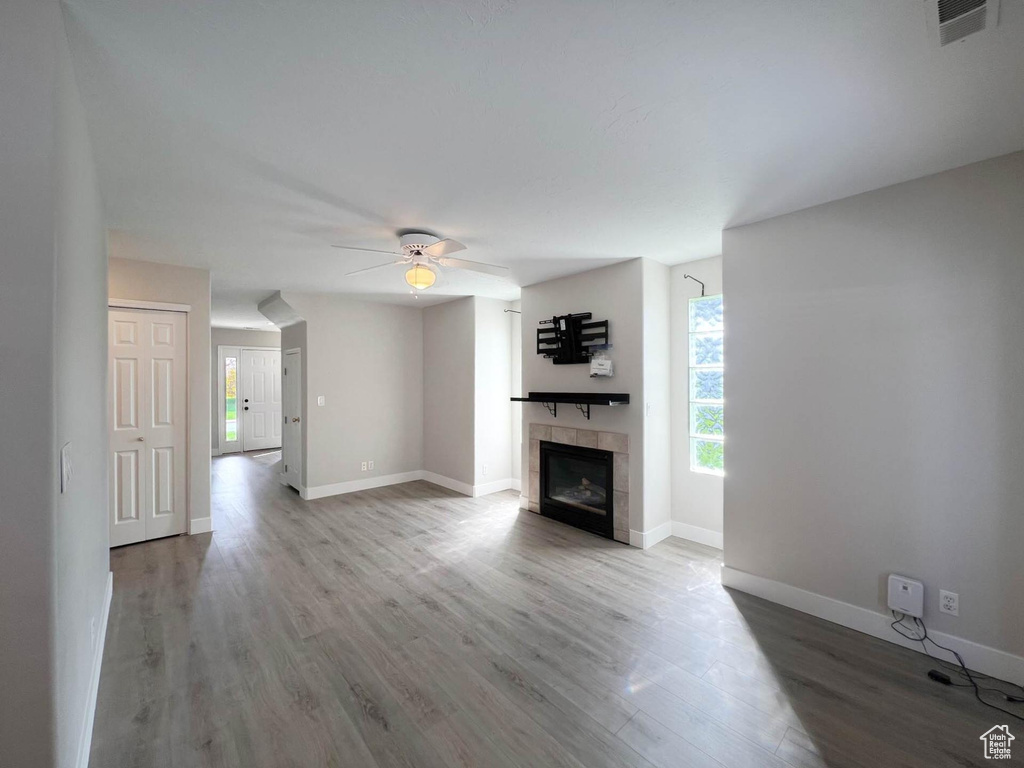 Unfurnished living room featuring a tiled fireplace, visible vents, ceiling fan, and wood finished floors