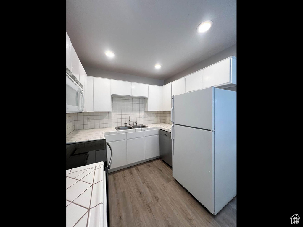 Kitchen with white cabinets, a sink, white appliances, light wood finished floors, and tile countertops