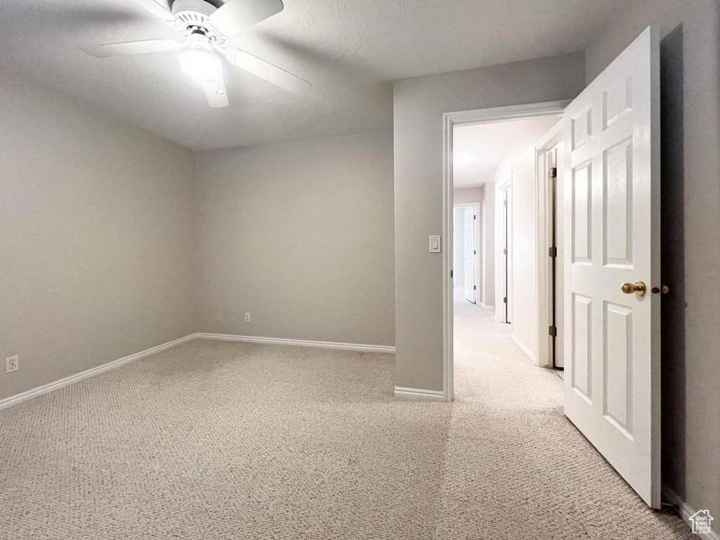 Empty room with light colored carpet, baseboards, and a ceiling fan