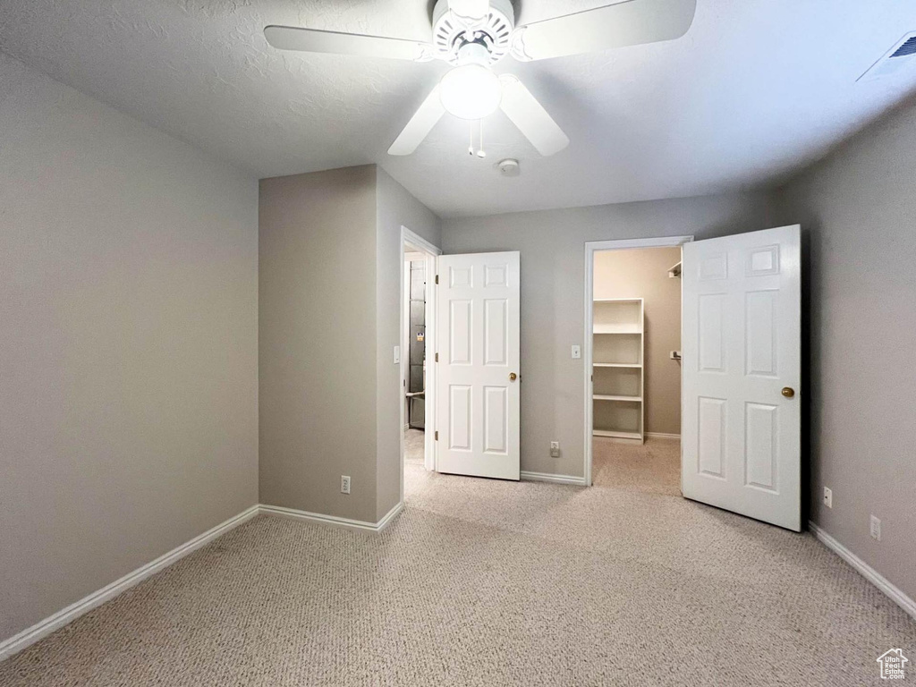 Unfurnished bedroom featuring baseboards, a walk in closet, visible vents, ceiling fan, and light colored carpet