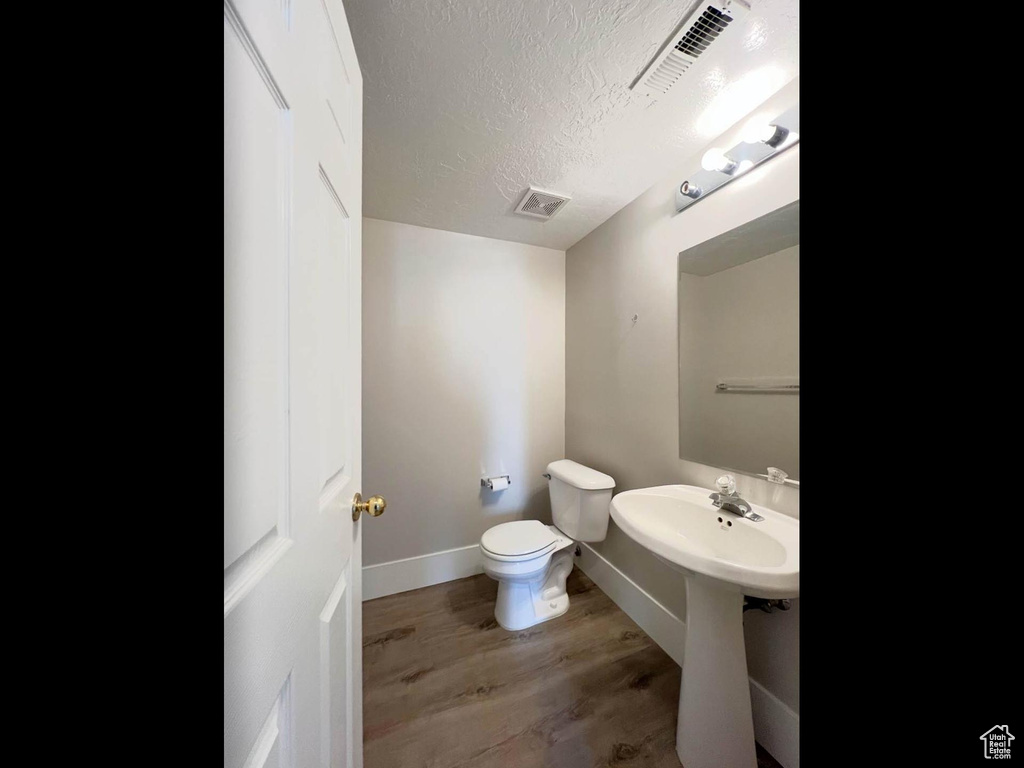 Half bath with visible vents, baseboards, toilet, a textured ceiling, and wood finished floors