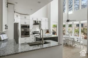 Kitchen featuring a sink, white cabinets, light stone countertops, appliances with stainless steel finishes, and wall chimney exhaust hood