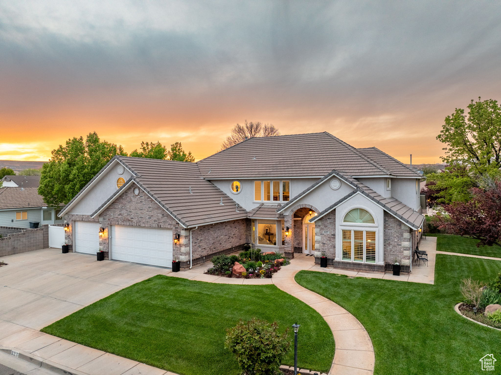 View of front facade with driveway, an attached garage, a tiled roof, and a yard