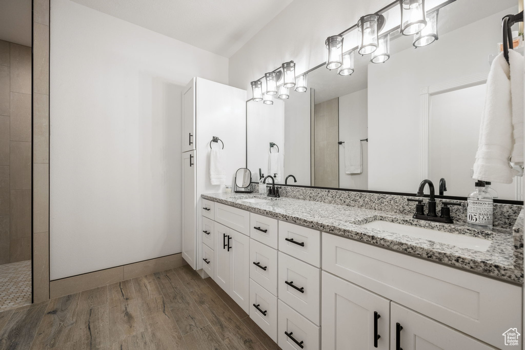 Bathroom with double vanity, a sink, a tile shower, and wood finished floors