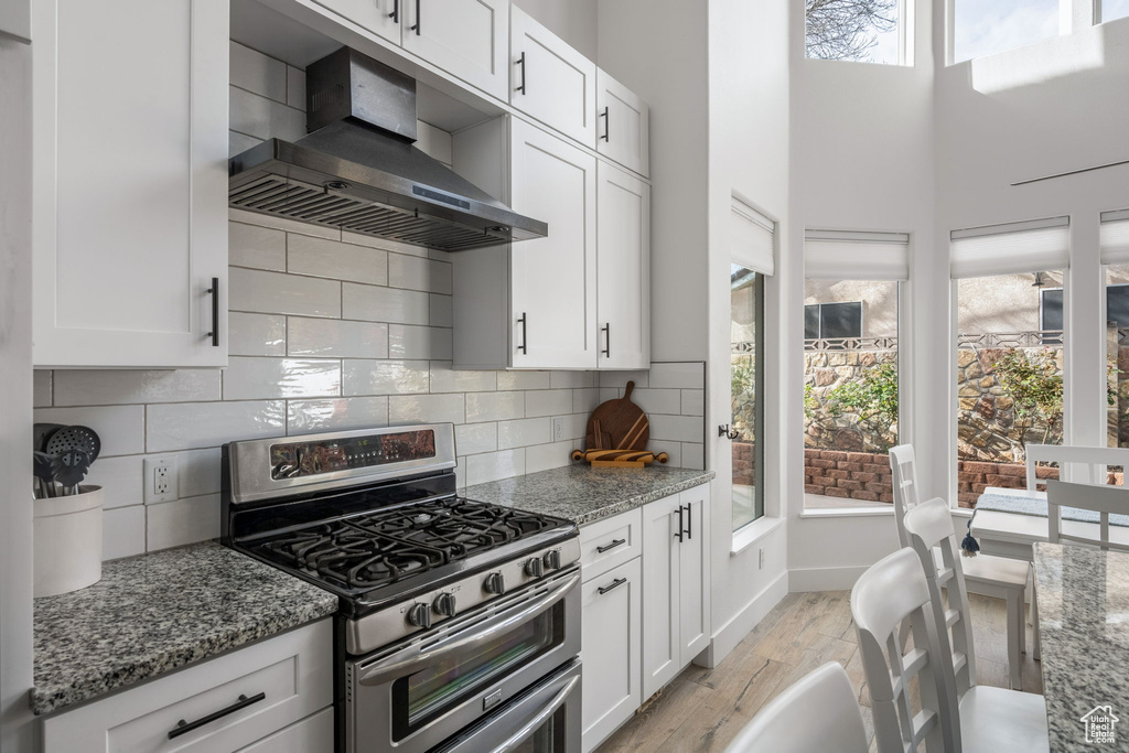 Kitchen with light stone countertops, white cabinetry, light wood-style floors, double oven range, and wall chimney range hood