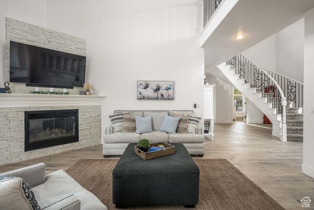 Living room featuring a high ceiling, a stone fireplace, stairs, and wood finished floors