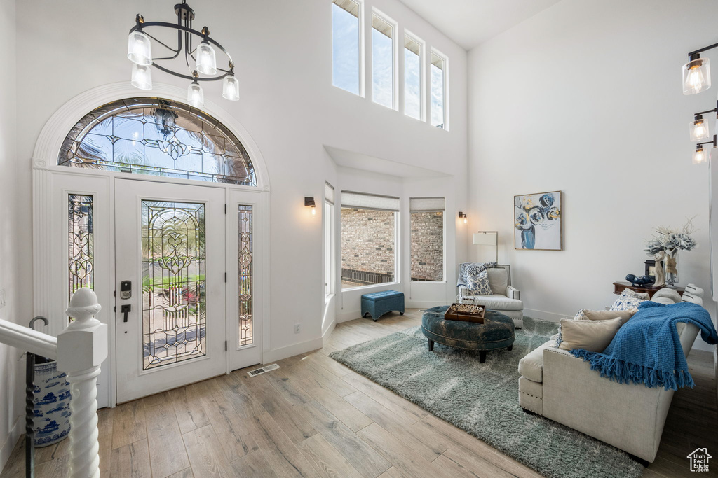 Entryway with a towering ceiling, a notable chandelier, visible vents, and wood finished floors