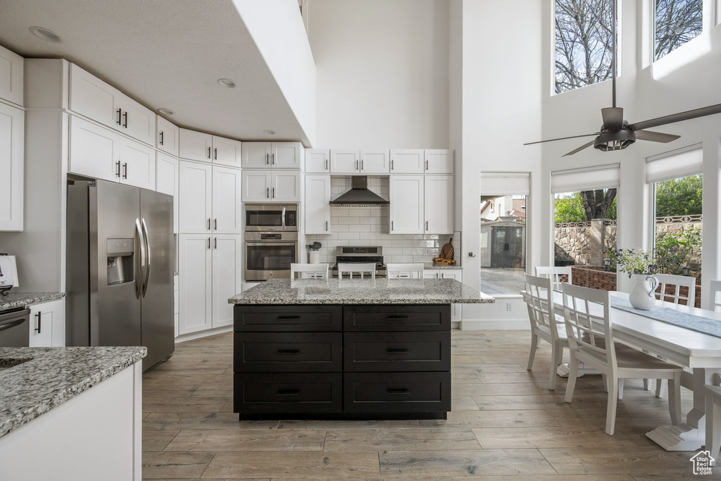 Kitchen with white cabinets, wall chimney range hood, stainless steel appliances, and light wood finished floors
