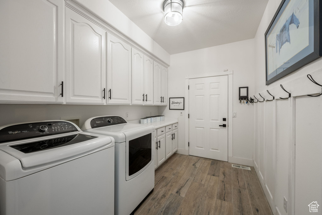 Washroom featuring baseboards, visible vents, cabinet space, washer and dryer, and wood finished floors