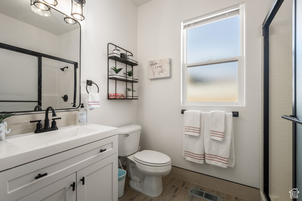 Full bath with visible vents, toilet, tiled shower, and wood finished floors