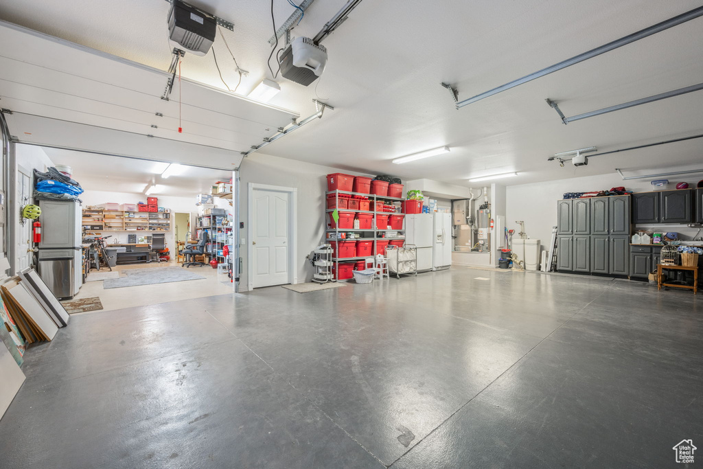 Garage featuring a workshop area, a garage door opener, and white fridge with ice dispenser