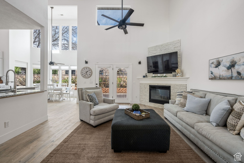 Living area featuring baseboards, ceiling fan, wood finished floors, a stone fireplace, and a high ceiling