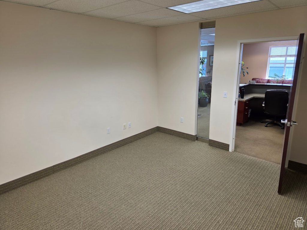Below grade area featuring carpet flooring, a drop ceiling, a desk, and baseboards